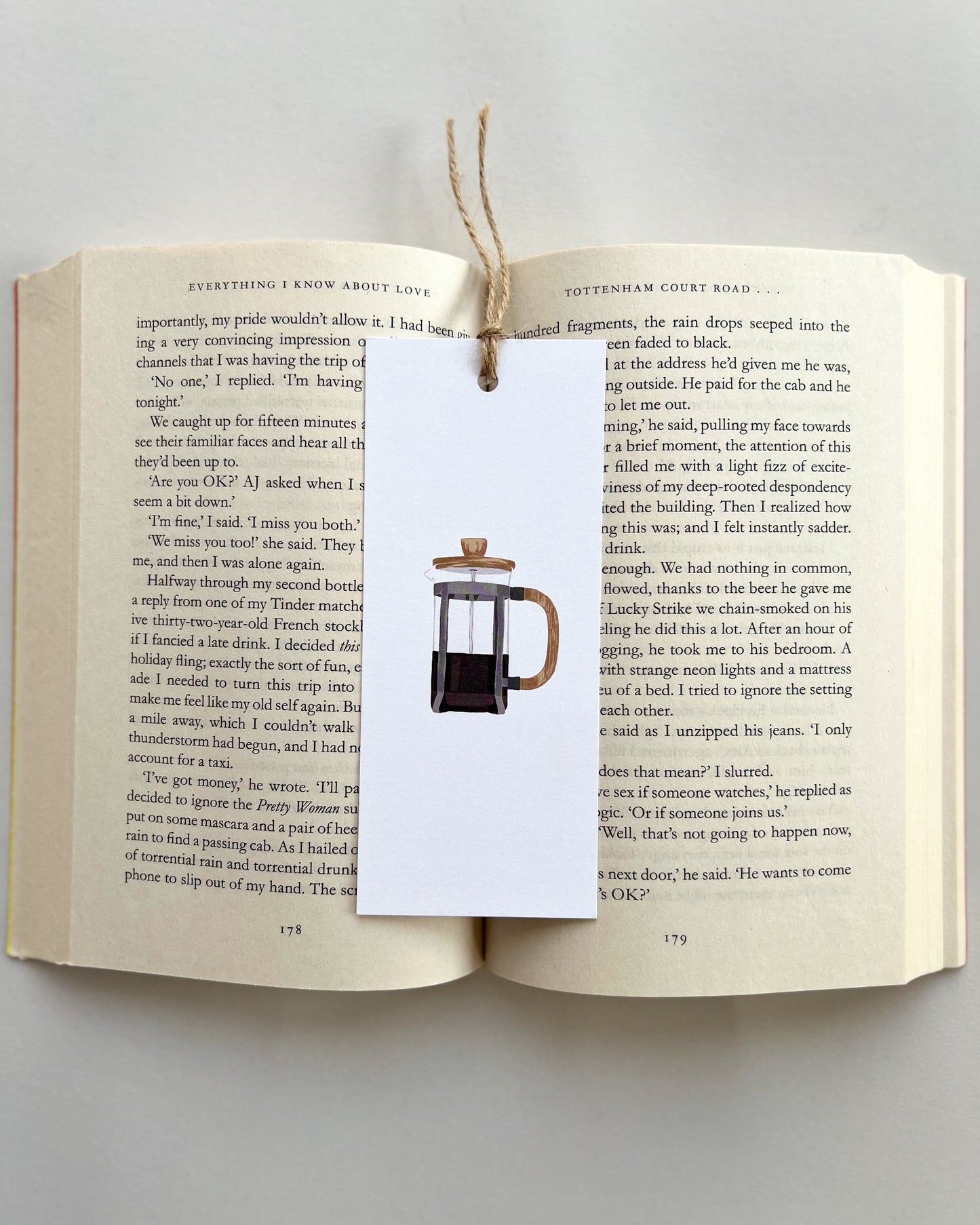 Open book with a bookmark featuring a coffee french press illustration on a light gray background