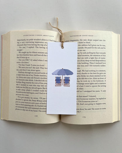 Open book with a bookmark featuring beach chairs and an umbrella on a white background