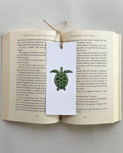 Open book with a turtle bookmark attached to a white card on a light gray background
