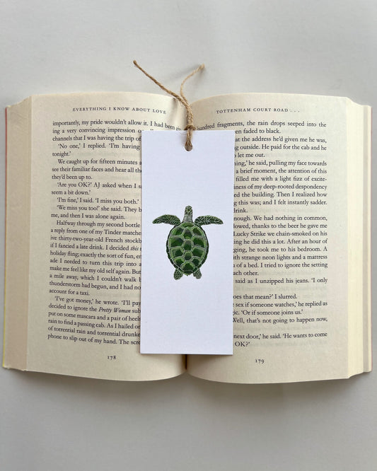 Open book with a turtle bookmark attached to a white card on a light gray background
